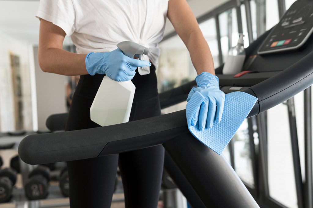 woman-with-gloves-cleaning-solution-disinfecting-gym-equipment